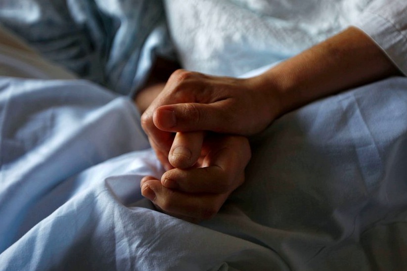 Two hands clasped in comfort on a hospice bed to reflect comprehensive end-of-life doula care focused on dignity, comfort, and companionship.